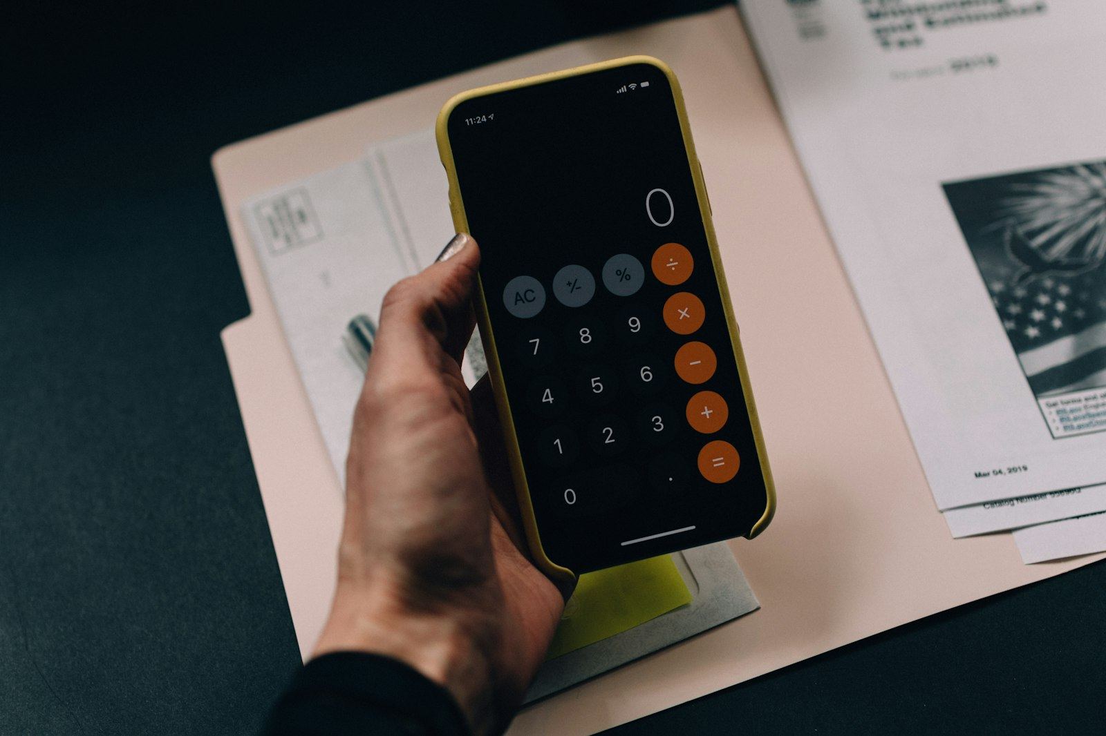 Hand som håller en mobiltelefon med miniräknaren öppen ovanför en mapp med räkningar